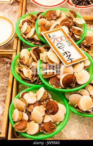 Le Japon, Kanazawa. Aliments frais Omi-cho marché couvert. Décrochage du poisson frais. Les crustacés, les palourdes dans des paniers en plastique vert avec étiquette de prix japonais. Banque D'Images
