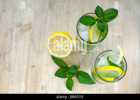 L'eau avec le citron, les feuilles de menthe et de la glace dans des verres en verre sur une table en bois. Citron, branches de menthe. Vue de dessus. Copiez l'espace. Cool l'eau detox Banque D'Images