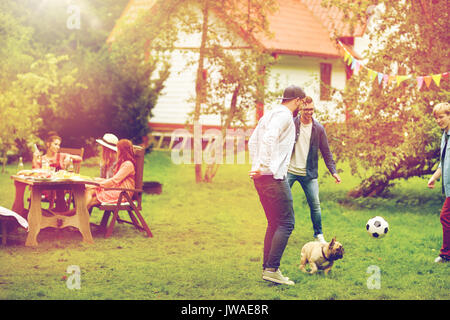 Les amis jouent au football avec chien au jardin d'été Banque D'Images