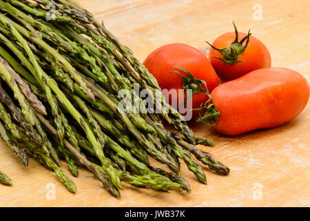 Un bouquet d'asperges avec les tomates sur une planche à découper en bois. Close up format paysage. Banque D'Images