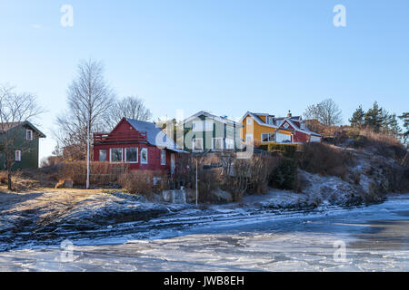 Cabines en bois de couleur sur l'île avec la mer gelée à l'avant-plan. Style scandinave Banque D'Images