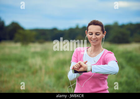 Femme d'âge moyen contrôler son sport ou de la santé regarder tandis que dehors le jogging dans la campagne à l'écoute de la musique sur son téléphone mobile dans une saine lifestyl Banque D'Images