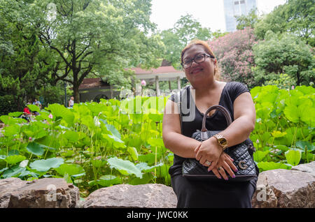 Une dame s'assoit et pose pour un portrait en face d'un bassin de fleurs de lotus dans People's Park à Shanghai, Chine. Banque D'Images