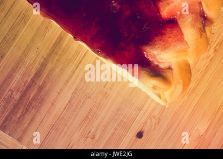 Un parfum frais et part de tarte avec un remplissage sucré de fraises cuites en gelée et repose sur une surface en bois. Banque D'Images