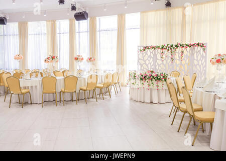 Chambre joliment décorée dans des tons pastel de blanc avec des tables couvertes de fleurs dans le restaurant pour la célébration du mariage d'intérieur. Banque D'Images