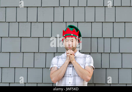 Homme qui prie avec un chapeau de Noël sur sur un arrière-plan gris. Banque D'Images