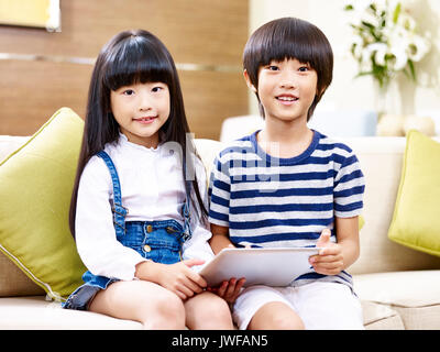 Portrait de deux enfants asiatiques sitting on couch holding digital tablet. Banque D'Images