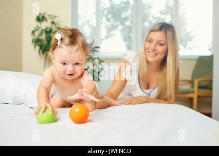 L'enfant joue avec ses jouets sur le lit avec sa mère. Banque D'Images