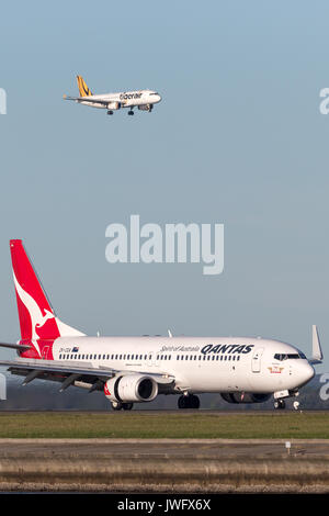 Boeing 737-800 de Qantas à l'aéroport de Sydney avec un Tiger Airways Airbus A320 en approche dans l'arrière-plan. Banque D'Images