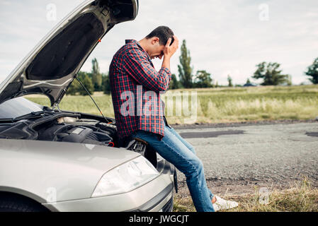 L'homme déprimé assis sur un capot de voiture. Véhicule avec ouvrir le capot sur la route Banque D'Images