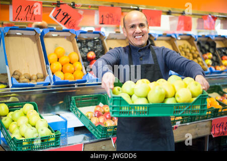 Portrait of happy smiling young man in apron vente de fruits de saison au marché intérieur Banque D'Images