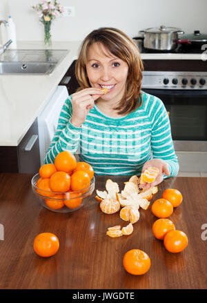 Happy woman eating tangerines à table en cuisine à domicile Banque D'Images