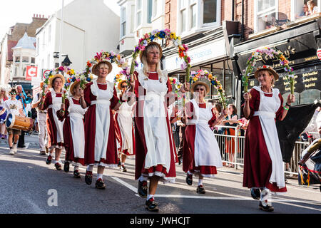 Défilé du festival de la semaine folklorique de Broadstairs. Folk Dancers, la montée de l'équipe femmes Alouettes Morris, marchant le long de la rue principale, tenant la moitié des guirlandes de fleurs au-dessus de têtes. Porter des robes orange avec tablier blanc, et des chapeaux de paille. Banque D'Images