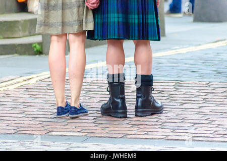 Edinburgh, Ecosse, Royaume-Uni. 12 août, 2017. Les jambes de deux personnes de l'arrière avec une jupe et des chaussures l'autre avec kilt et docteur martin bottes, tenant les mains, sur les rues pavées de la ville à la fin de la première semaine de la 70e anniversaire de l'Edinburgh International Fringe Festival. Credit : Skully/Alamy Live News Banque D'Images