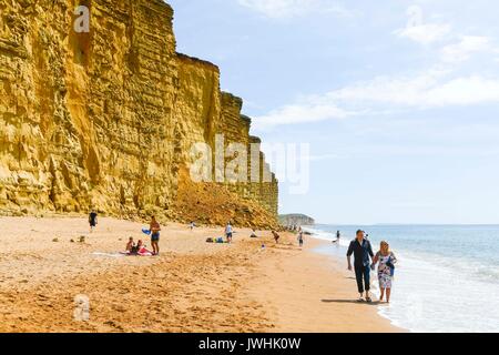 West Bay, Dorset, UK. 13 août 2017. Météo britannique. Les vacanciers appréciant une promenade le long de la plage à la station balnéaire de West Bay, dans Dorset sur une chaude journée ensoleillée. Crédit photo : Graham Hunt/Alamy Live News Banque D'Images