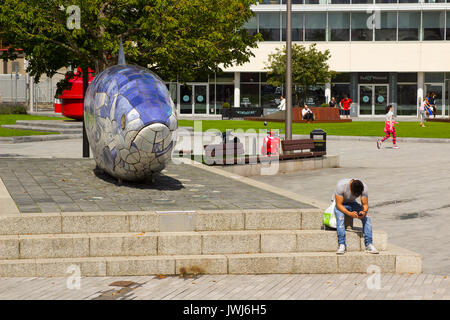 Un jeune homme assis à côté de texter le gros poisson sculpture sur le Donegall Quay dans la zone du port de Belfast, en Irlande du Nord Banque D'Images