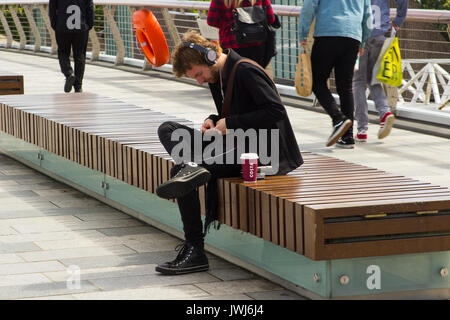 Un jeune homme en utilisant son téléphone mobile tout en vous relaxant au bord de l'eau at Belfast's River Lagan. Banque D'Images