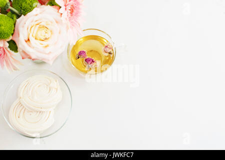 Une tasse de thé à base de plantes en bonne santé avec des roses séchées. De magnifiques fleurs fraîches, une meringue française des cookies sur light table en marbre, vue d'en haut. Gerbera rose et roses Banque D'Images