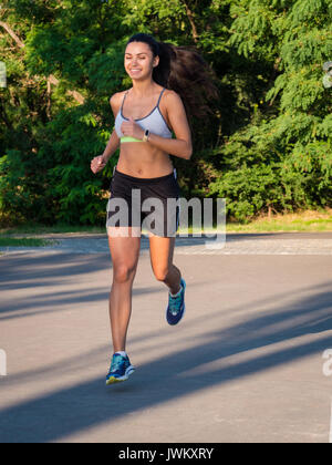 Fille court à travers le parc dans la matinée. Jeune sportive attractive brunette woman Running on Empty Road dans la matinée. Banque D'Images