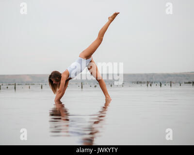 Young caucasian woman in swimsuit pratiquant le yoga dans l'eau liman, lac ou rivière. Belle réflexion. Asanas complexes, de l'équilibre. Sport, Fitness, yoga un Banque D'Images