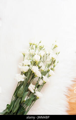 Un gros bouquet de fleurs blanches sur le plancher de bois sur un tapis de fourrure blanche. Confortable, confortable maison de mode la féminité. Mise à plat de style. Vue d'en haut, l'image verticale Banque D'Images