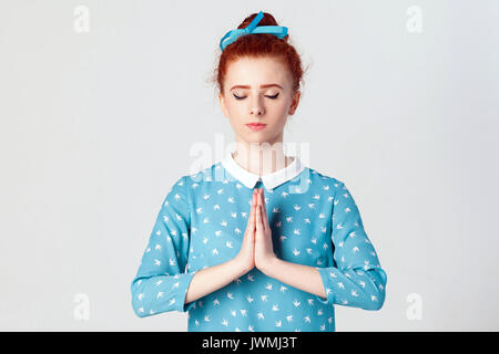 Magnifique jeune femme rousse caucasiens, holding hands in namaste ou prière, gardant les yeux fermés tout en pratiquant le yoga et la méditation à la maison seul, h Banque D'Images
