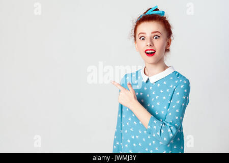 Les jeunes excités redhead caucasian girl avec noeud de cheveux pointant son index sur le côté, soulevant les sourcils et garder la bouche grande ouverte, montrant someth Banque D'Images