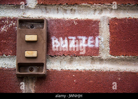 Vieux métal rouillé buzzer sur un mur de brique avec le mot en manuscrit peint sur le Buzzer en briques lettrage blanc Banque D'Images