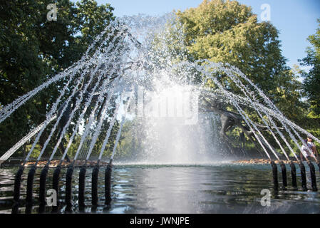 Fontaine ornementale avec des jets d'eau d'arc de buses haute pression formant un affichage sur un étang dans un parc boisé Banque D'Images