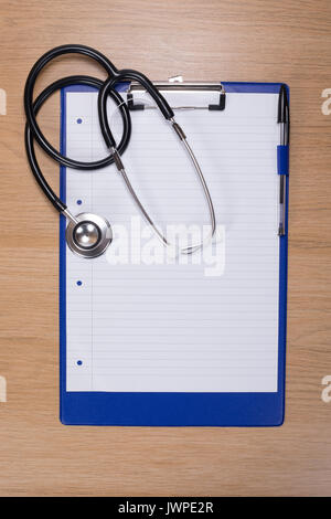 Stéthoscope posé sur une presse-papiers avec le papier blanc sur un bureau en bois (vue de dessus dans un concept de santé Banque D'Images