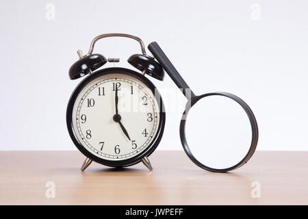 Petite loupe ronde appuyé contre un vieux réveil avec sonnerie sur une table en bois avec copie espace sur un mur blanc Banque D'Images