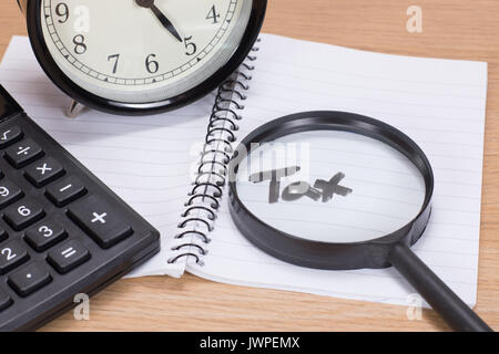 Date limite d'impôt concept avec une loupe sur le texte manuscrit dans un ordinateur portable et d'un réveil et une calculatrice sur un bureau en bois Banque D'Images