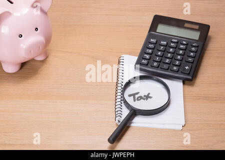 Calcul de l'impôt et de l'analyse avec un concept pink piggy bank, calculatrice et loupe, couché sur un bloc-notes sur le mot en manuscrit - Fiscalité - sur un Banque D'Images