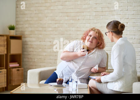 Portrait of young woman eating cupcakes obèses et souriant pendant la thérapie avec un psychiatre femelle Banque D'Images