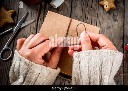 Préparation pour l'automne et d'hiver. La personne qui emballe les cookies comme un cadeau dans un métier fort, ruban de Noël, les mains dans le châssis. Lo rustique Banque D'Images