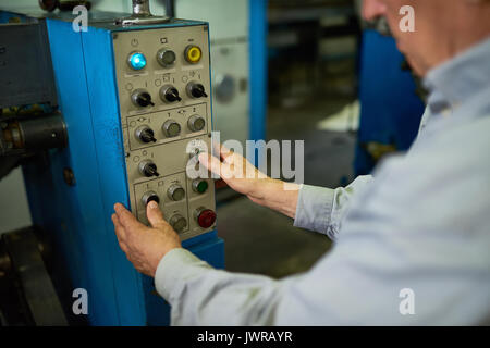 Gros plan du méconnaissable senior man l'utilisation de machines en usine, les mains appuyant sur les boutons du panneau de contrôle. Banque D'Images