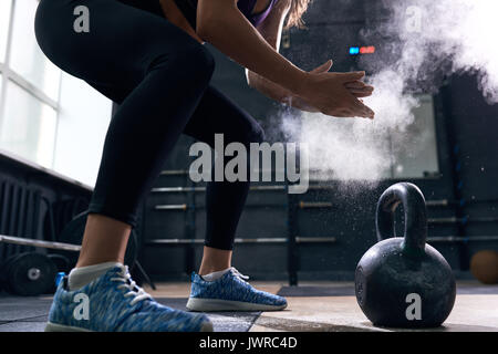 Gros plan Vue de côté d'méconnaissable jeune femme lui frottait les mains à parler que quelques bouffées cloud préparez à soulever au cours d'entraînement Crossfit kettlebells en mod Banque D'Images