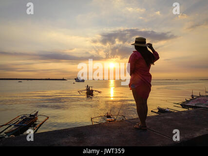 Une femme debout et regardant le coucher du soleil dans la baie de Manille, Philippines. Banque D'Images