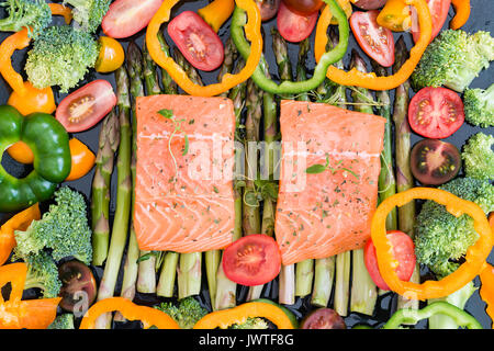 Deux morceaux de filet de saumon cru sur matières premières asperges vertes, tomates cerises, poivrons, brocoli et sur la plaque de cuisson garnie de thym frais. Ingrédients Banque D'Images