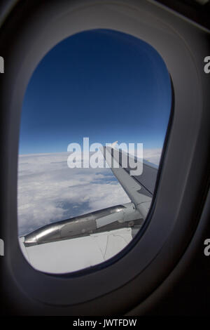 Vue verticale de la fenêtre de l'avion et l'aile avec les nuages au-dessous et au-dessus de ciel bleu Banque D'Images