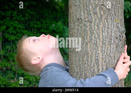 Garçon avec le syndrome de Down à la vers le ciel et l'enlaça d'un arbre. Banque D'Images