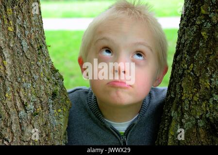 Garçon avec le syndrome de Down à la vers le ciel et l'enlaça d'un arbre. Banque D'Images