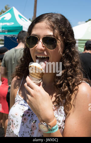 Belle jeune femme aux cheveux bruns frisés eating ice cream au Festival Austin Ice Cream fond pittoresques en plein air avec des foules et des parasols. Banque D'Images