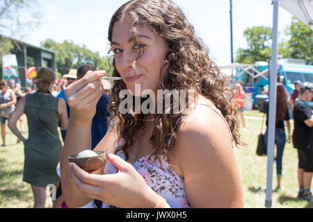 Belle jeune femme aux cheveux bruns frisés eating ice cream au Festival Austin Ice Cream fond pittoresques en plein air avec des foules et des parasols. Banque D'Images