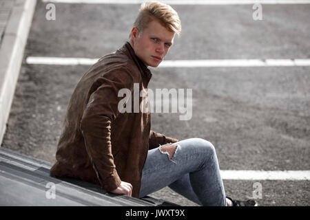 Jeune rousse homme en veste brune posant contre le mur. Banque D'Images