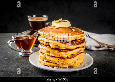 La cuisine traditionnelle d'automne. Pile de crêpes à la citrouille avec du beurre, les graines de citrouille et sirop d'érable. Avec une tasse de café. Sur une table en pierre noire. Copier sp Banque D'Images