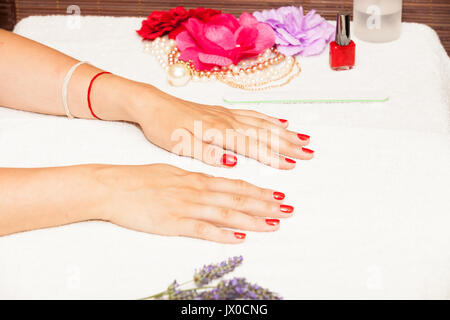 Les mains d'une femme avec des vernis à ongles rouge posé par l'esthéticienne Banque D'Images