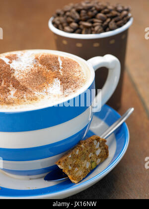 Cappuccino dans grand mug bleu et blanc avec de la cannelle avec vente à emporter tasse pleine de haricots ,Journal et biscotti Banque D'Images