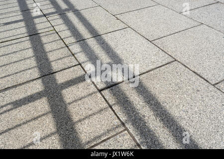Ombres des mains courantes métalliques tombant sur les lignes de pavés. Pavés, pavés. Métaphore de la place publique. Banque D'Images