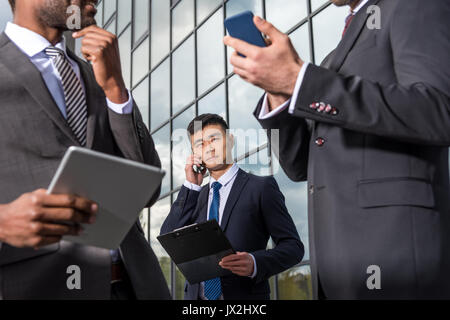 Réunion de l'équipe d'entreprises multiculturelles et à l'aide de smartphones et tablettes numériques à l'extérieur près de l'immeuble de bureaux Banque D'Images